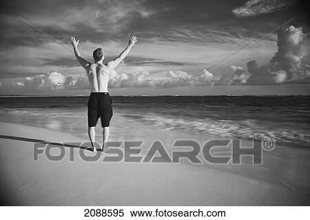 A man stands on a wet beach with arms raised looking out at the ocean; punta cana la altagracia dominican republic View Large Photo Image Stock Photography - A man stands on a wet beach with arms raised looking out at the ocean; punta cana la altagracia dominican republic. Fotosearch