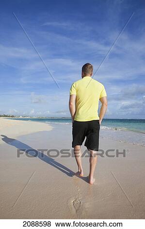 Stock Photo - A man walks on the wet beach; punta cana la altagracia dominican republic. Fotosearch