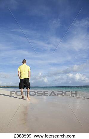 Stock Photo - A man walks on the wet beach; punta cana la altagracia dominican republic. Fotosearch