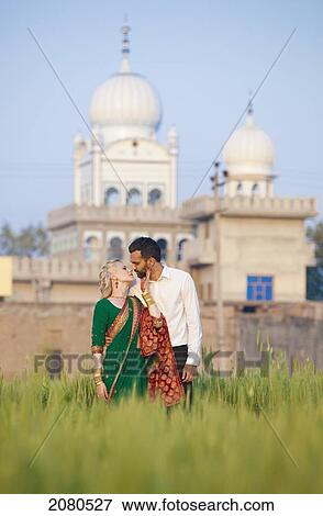 A mixed race couple her wearing a sari face to face in a field with a temple in the background; ludhiana punjab india View Large Photo Image Stock Photo - A mixed race couple her wearing a sari face to face in a field with a temple in the background; ludhiana punjab india. Fotosearch