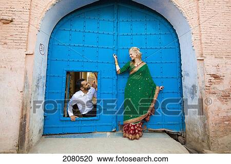 Stock Image - A mixed race couple with her wearing a sari at a doorway with large blue doors; ludhiana punjab india. Fotosearch