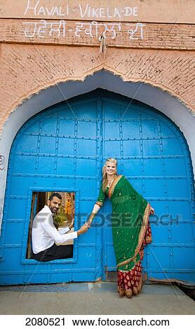 Stock Image - A mixed race couple with her wearing a sari at a doorway with large blue doors; ludhiana punjab india. Fotosearch
