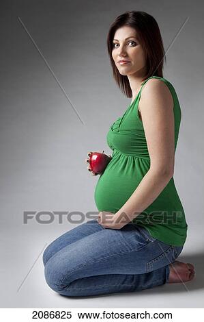 Stock Photography - A pregnant woman holding an apple beside her pregnant belly; edmonton alberta canada. Fotosearch