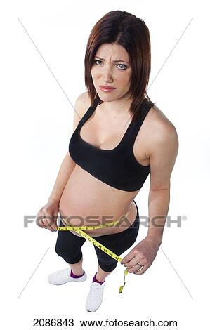 Stock Image - A pregnant woman holds a measuring tape around her bare pregnant belly; edmonton alberta canada. Fotosearch
