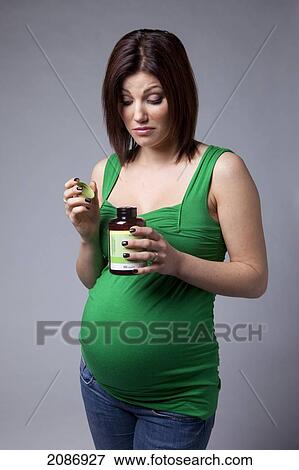 Stock Photo - A pregnant woman looks curiously into an open bottle of vitamins; edmonton alberta canada. Fotosearch