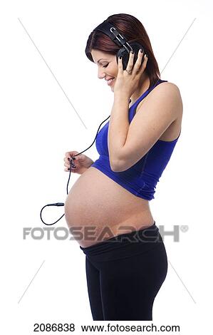 Stock Photo - A pregnant woman with a headset plugged into her belly to hear the sounds of her unborn baby; edmonton alberta canada. Fotosearch