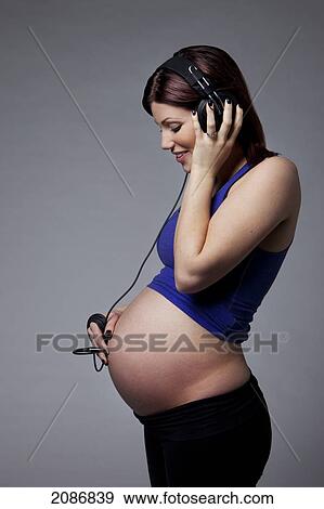 Stock Photo - A pregnant woman with a headset plugged into her belly to hear the sounds of her unborn baby; edmonton alberta canada. Fotosearch