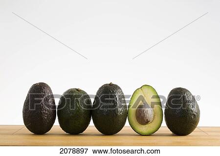 A row of avocados standing upright on a wooden board with one cut in half with the pit; calgary alberta canada View Large Photo Image Stock Photo - A row of avocados standing upright on a wooden board with one cut in half with the pit; calgary alberta canada. Fotosearch