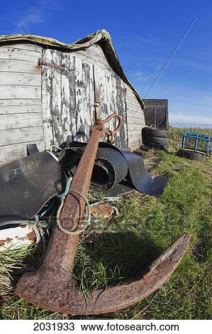 Stock Image - A Rusted Anchor Lays On The Grass Beside A Weathered Building; Holy Island Northumberland England. Fotosearch