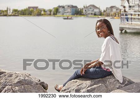 A Teenage Girl Relaxing On The Rocks On Shore Of A Residential Lake; Edmonton Alberta Canada View Large Photo Image Stock Image - A Teenage Girl Relaxing On The Rocks On Shore Of A Residential Lake; Edmonton Alberta Canada. Fotosearch