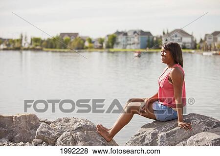 A Teenage Girl Relaxing On The Rocks On Shore Of A Residential Lake; Edmonton Alberta Canada View Large Photo Image Stock Photo - A Teenage Girl Relaxing On The Rocks On Shore Of A Residential Lake; Edmonton Alberta Canada. Fotosearch