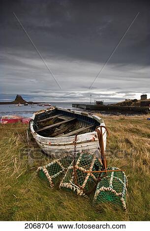 A Weathered Boat And Fishing Equipment Sitting On The Shore With Lindisfarne Castle In The Distance; Lindisfarne Northumberland England View Large Photo Image Picture - A Weathered Boat And Fishing Equipment Sitting On The Shore With Lindisfarne Castle In The Distance; Lindisfarne Northumberland England. Fotosearch