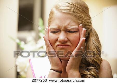 Stock Image - A woman holding her face in her hands with an unpleasant expression; grand junction colorado united states of america. Fotosearch