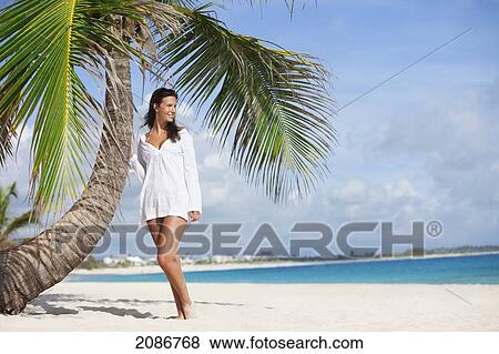 A woman in a white dress posing beside a palm tree on a beach; punta cana la altagracia dominican republic View Large Photo Image Stock Photo - A woman in a white dress posing beside a palm tree on a beach; punta cana la altagracia dominican republic. Fotosearch