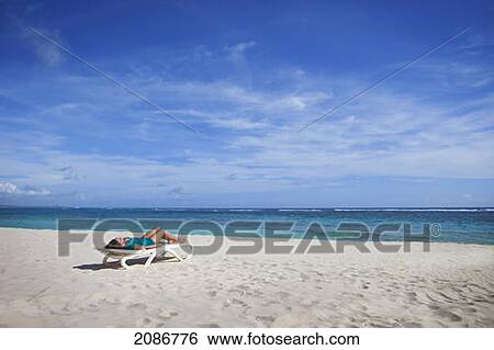 A woman lays on a lounge chair on the white sand beach at the water's edge; punta cana la altagracia dominican republic View Large Photo Image Stock Photograph - A woman lays on a lounge chair on the white sand beach at the water's edge; punta cana la altagracia dominican republic. Fotosearch