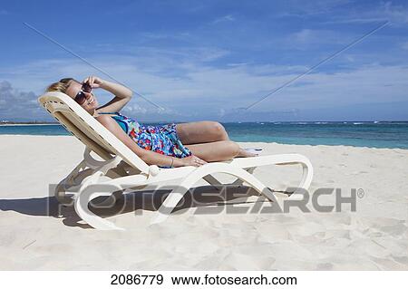 Stock Photo - A woman relaxing on a beach chair by the ocean; punta cana la altagracia dominican republic. Fotosearch