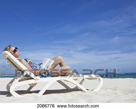 Stock Photo - A woman relaxing with a book on a beach chair by the ocean; punta cana la altagracia dominican republic. Fotosearch
