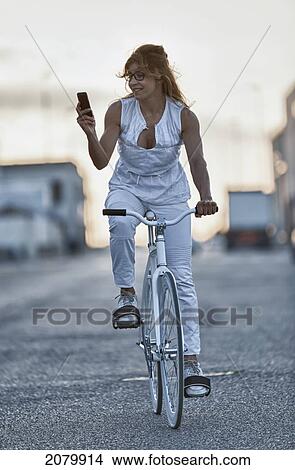 Picture - A woman riding her bike and checking her cell phone; tarifa cadiz andalusia spain. Fotosearch