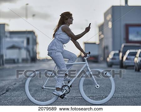 Stock Photo - A woman riding her bike and using her cell phone while crossing the street; tarifa cadiz andalusia spain. Fotosearch