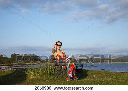 A Woman Sitting At The Water's Edge Reading A Book At Parknasilla Near Sneem; County Kerry Ireland View Large Photo Image Stock Photograph - A Woman Sitting At The Water's Edge Reading A Book At Parknasilla Near Sneem; County Kerry Ireland. Fotosearch