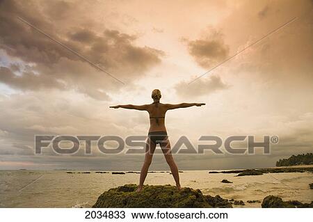 A Woman Tourist Wearing A Bikini Raises Her Arms And Does Yoga On The Beach Of A Tropical Island At Sunset; Koh Lanta Thailand View Large Photo Image Stock Image - A Woman Tourist Wearing A Bikini Raises Her Arms And Does Yoga On The Beach Of A Tropical Island At Sunset; Koh Lanta Thailand. Fotosearch