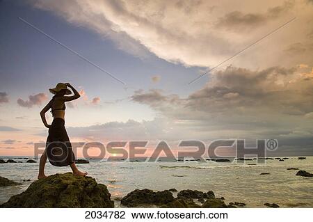 A Woman Tourist Wearing A Hat And Sarong Stands On The Beach Of A Tropical Island At Sunset; Koh Lanta Thailand View Large Photo Image Stock Image - A Woman Tourist Wearing A Hat And Sarong Stands On The Beach Of A Tropical Island At Sunset; Koh Lanta Thailand. Fotosearch