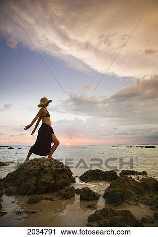 A Woman Tourist Wearing A Hat And Sarong Stands On The Beach Of A Tropical Island At Sunset; Koh Lanta Thailand View Large Photo Image Stock Image - A Woman Tourist Wearing A Hat And Sarong Stands On The Beach Of A Tropical Island At Sunset; Koh Lanta Thailand. Fotosearch