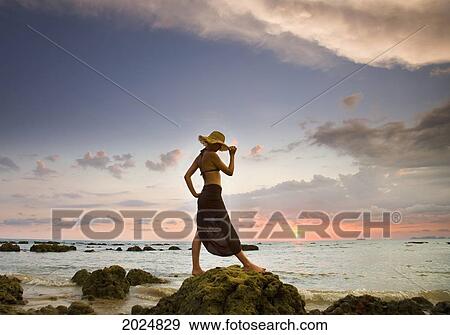 A Woman Wearing A Hat And Sarong Stands On The Beach Of A Tropical Island At Sunset; Koh Lanta Krabi Province Thailand View Large Photo Image Stock Photo - A Woman Wearing A Hat And Sarong Stands On The Beach Of A Tropical Island At Sunset; Koh Lanta Krabi Province Thailand. Fotosearch