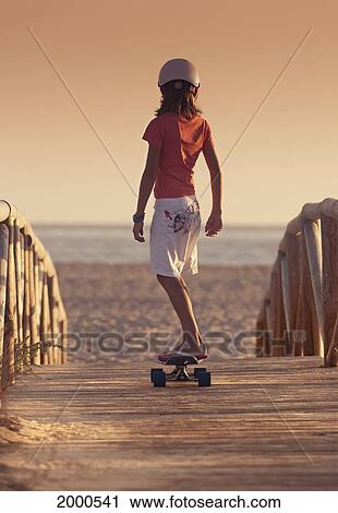 Stock Image - A Young Person Skateboarding With Bare Feet Over A Wooden Boardwalk Towards The Beach; Tarifa Cadiz Andalusia Spain. Fotosearch