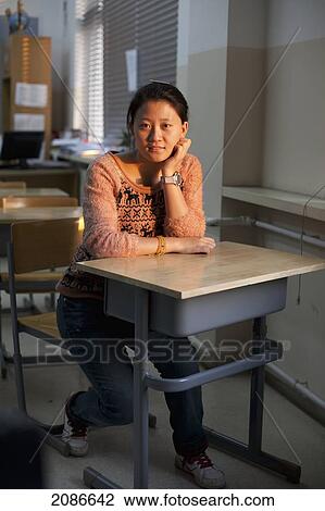 Stock Image - A young woman sits at a desk in a classroom; beijing china. Fotosearch