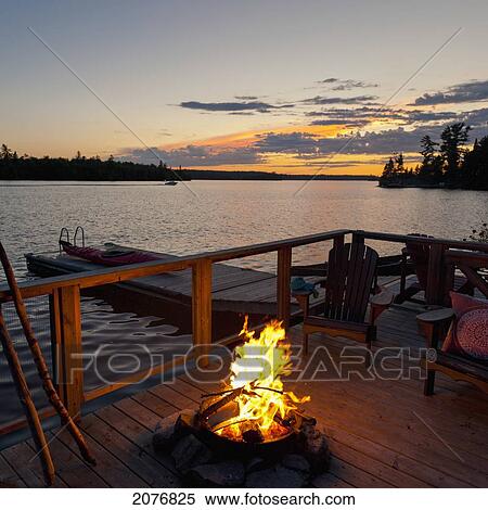 Stock Photography - Burning fire on a wooden dock along the water's edge at sunset; lake of the woods ontario canada. Fotosearch
