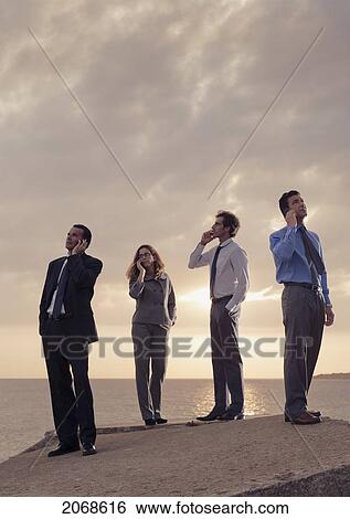 Businessmen And A Businesswoman Using Their Cell Phones While Standing At The Water's Edge; Tarifa Cadiz Andalusia Spain View Large Photo Image Stock Photograph - Businessmen And A Businesswoman Using Their Cell Phones While Standing At The Water's Edge; Tarifa Cadiz Andalusia Spain. Fotosearch