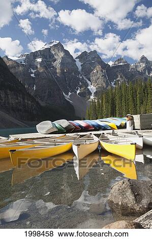 Canoes Along A Dock Reflecting Off The Lake With Mountains Clouds And Blue Sky; Alberta Canada View Large Photo Image Stock Photo - Canoes Along A Dock Reflecting Off The Lake With Mountains Clouds And Blue Sky; Alberta Canada. Fotosearch