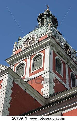 Stock Image - Clock and gold cross on the top of a red building; stockholm sweden. Fotosearch