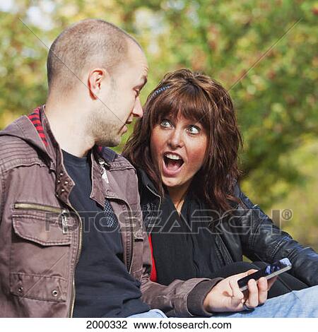 Stock Image - Couple Looking At Text Messages In The Park; Edmonton Alberta Canada. Fotosearch