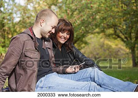 Stock Image - Couple Looking At Text Messages In The Park; Edmonton Alberta Canada. Fotosearch