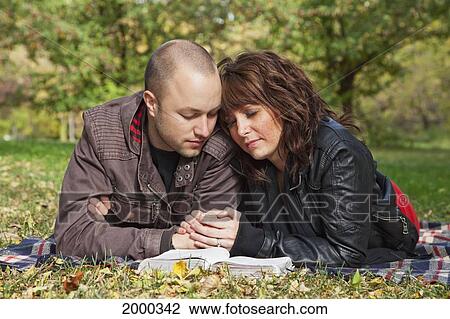 Stock Image - Couple Reading Bible And Praying Together In A Park; Edmonton Alberta Canada. Fotosearch