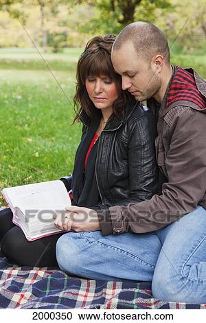 Stock Image - Couple Reading Bible And Praying Together In The Park; Edmonton Alberta Canada. Fotosearch