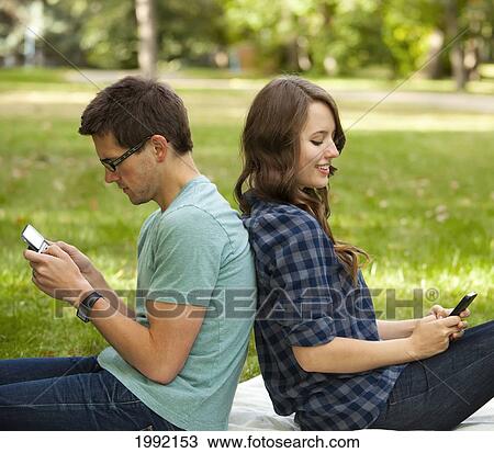 Stock Image - Couple Texting In A Park; Edmonton Alberta Canada. Fotosearch