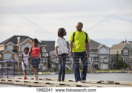 Stock Image - Father And Daughters Walking And Talking On A Pier In A Residential Lake Area; Edmonton Alberta Canada. Fotosearch