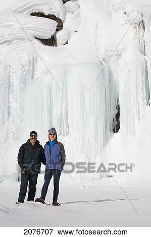 Female and male snowshoers in front of a frozen ice wall and snow covered cliff; alberta canada View Large Photo Image Stock Photo - Female and male snowshoers in front of a frozen ice wall and snow covered cliff; alberta canada. Fotosearch