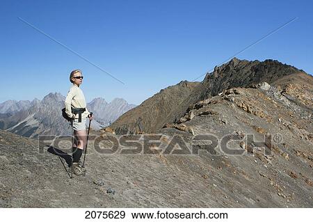Female Hiker On Top Of Mountain Ridge With Hiking Poles And Mountains In The Distance With Blue Sky; Alberta Canada View Large Photo Image Stock Photo - Female Hiker On Top Of Mountain Ridge With Hiking Poles And Mountains In The Distance With Blue Sky; Alberta Canada. Fotosearch