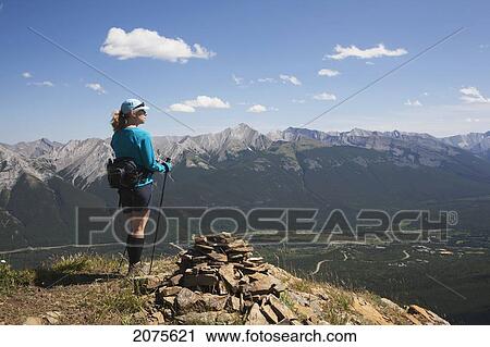 Female Hiker With Hiking Poles Standing On Rocky Top Overlooking Mountains And Valley In The Distance With Blue Sky And Clouds; Alberta Canada View Large Photo Image Stock Image - Female Hiker With Hiking Poles Standing On Rocky Top Overlooking Mountains And Valley In The Distance With Blue Sky And Clouds; Alberta Canada. Fotosearch