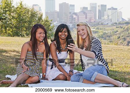 Stock Photo - Friends Looking At Smart Phones In A City Park With The Skyline In The Background; Edmonton Alberta Canada. Fotosearch