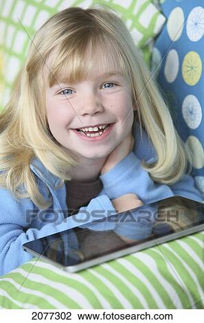 Stock Image - Girl laying on a couch playing with a tablet; troutdale oregon united states of america. Fotosearch