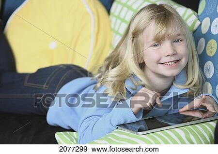 Girl laying on a couch playing with a tablet; troutdale oregon united states of america View Large Photo Image Stock Photo - Girl laying on a couch playing with a tablet; troutdale oregon united states of america. Fotosearch
