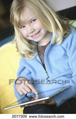 Girl sitting on a couch playing with a tablet; troutdale oregon united states of america View Large Photo Image Stock Photo - Girl sitting on a couch playing with a tablet; troutdale oregon united states of america. Fotosearch
