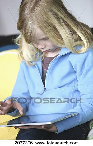 Girl sitting on a couch playing with a tablet; troutdale oregon united states of america View Large Photo Image Stock Photograph - Girl sitting on a couch playing with a tablet; troutdale oregon united states of america. Fotosearch