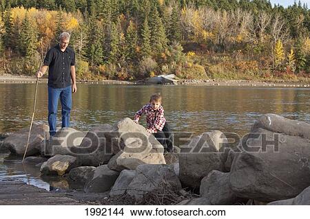 Picture - Grandfather And Grandson Playing Along The Rocks At The River's Edge; Edmonton Alberta Canada. Fotosearch