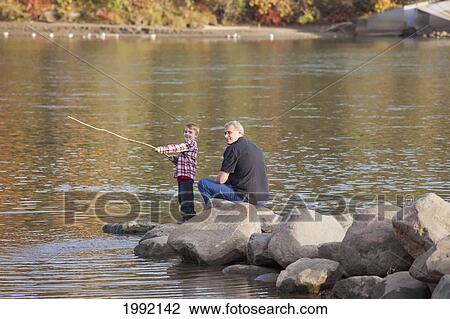 Stock Image - Grandfather And Grandson Playing Along The Rocks At The River's Edge; Edmonton Alberta Canada. Fotosearch